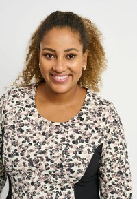 Langærmet bluse med et pink, sort og creme farvet prikket mønster, med en sort sidesøm og en rund halsudskæring. Blødt stof.