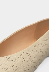 Μπεζ επίπεδη μπαλαρίνα με διάτρητα γεωμετρικά μοτίβα αστεριού και λεία εσωτερική επένδυση.