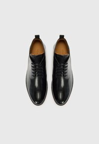 Zapatos de vestir de cuero negro con un acabado suave, puntera redonda, diseño de cordones y un forro interior de color marrón claro. Presentan una pequeña lengüeta en el talón.