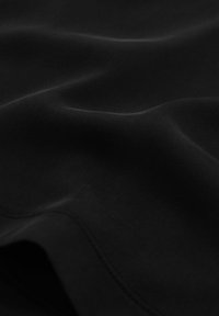 Primo piano di tessuto nero liscio con pieghe morbide e una trama sottile, che mette in risalto la lucentezza e il contorno con poca luce.