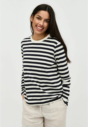 La camicia a maniche lunghe presenta righe orizzontali bianche e nere, un tessuto leggero, un collo rotondo e una vestibilità comoda, abbinata a pantaloni chiari.
