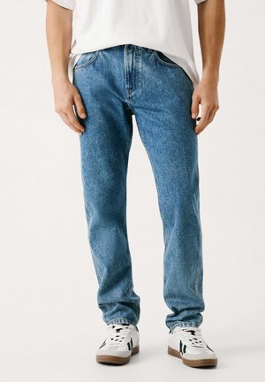Lys blå denimjeans med rett passform, falmet tekstur, fem-lomme design og knappestolpe, kombinert med hvite sneakers.