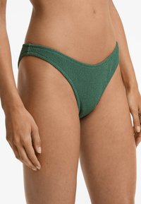 Costume da bagno verde testurizzato con taglio a vita bassa, caratterizzato da strisce laterali strette e un design senza cuciture per una finitura liscia.