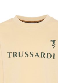 Kremowy sweatshirt z okrągłym dekoltem, z napisem "TRUSSARDI" w kolorze zielonym oraz zielonym logo po lewej stronie. Miękka faktura materiału.