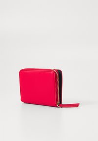 Portefeuille en cuir rouge avec une forme carrée, fermeture zippée et finition texturée. Équipé de quincaillerie dorée et d'une petite dragonne.