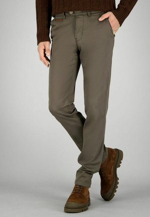 Khaki broek met een gladde textuur en een taps toelopende pasvorm. Voorzien van een knoopsluiting en voorzakken. Gecombineerd met bruine suède schoenen.