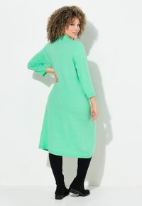 Abito a maglia verde menta, lungo fino al ginocchio, con maniche a tre quarti e vestibilità rilassata. Abbinato a stivali neri al ginocchio con una texture liscia.