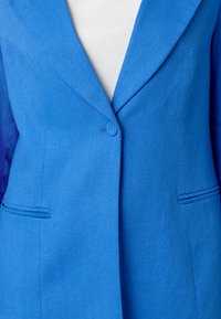 Blue herringbone blazer featuring a single button closure, notch lapel, and two front pockets. Smooth texture with tailored fit.