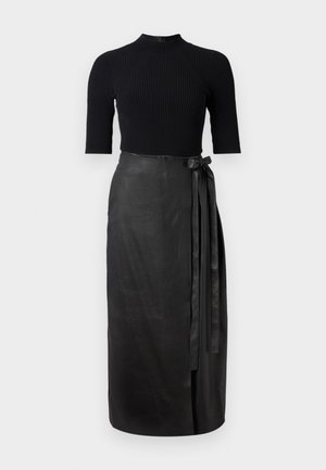 Zwart geribbelde top met korte mouwen, gecombineerd met een hoog-gewogen zwarte leren wikkelrok die aan de zijkant met een strik is vastgebonden.