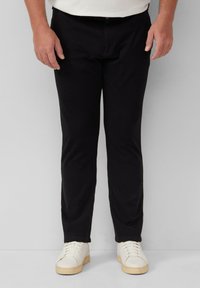 Schwarze Hosen mit geradem Bein, aus einem glatten Stoff gefertigt. Mit einem Knopf- und Reißverschluss, kombiniert mit weißen Sneakers.