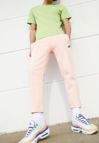 Světlé zelené tričko, slim-fit růžové tepláky s černým logem a multikolorové tenisky s bílými akcenty a fialovými tkaničkami.