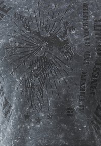 Gray, short-sleeved T-shirt with a faded texture. Features a large black graphic of a bird and text, with star accents at the bottom.