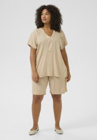 Haut en lin beige à col V avec des manches courtes, associé à un short assorti à mi-cuisse. Chaussures légères à enfiler.