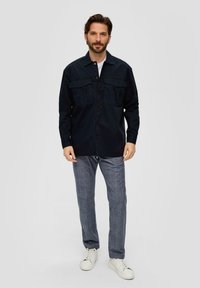 Camicia blu con bottoni, dotata di due tasche sul petto, abbinata a pantaloni a quadri grigi chiari e sneaker bianche. Tessuto morbido con una vestibilità comoda.