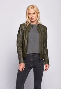 Olivgrön läderjacka med ståkrage, dragkedja framtill och sidofickor, tillsammans med en grå topp och svarta jeans.