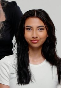 Des cheveux longs, droits et foncés sont mouillés et légèrement en désordre. Le sujet porte une chemise blanche simple, avec un fond neutre et une autre silhouette partiellement visible.