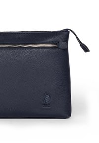Mörkblå läderpåse med texturerad yta. Har en dragkedja framtill och präglad logotyp. Designen är stilren med minimal hårdvara.