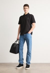 Svart polo skjorte, blå jeans, svarte joggesko, holder en svart lær veske. Korte ermer, klassisk passform, uformelt design, jevn tekstur.