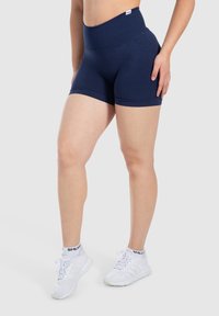 Shorts atléticos de cintura alta en color marino, fabricados con un material elástico, que presentan una textura suave y un ajuste ceñido, combinados con zapatillas deportivas blancas.