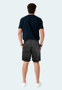 Schwarze Denim-Shorts mit umgeschlagenen Säumen, kombiniert mit einem dunkelblauen T-Shirt. Leichtes Material, einfaches Design und lässige Passform.