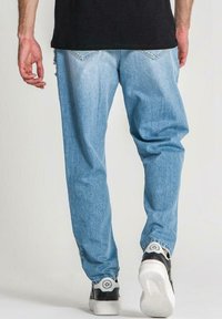 Vaaleansiniset farkut, jotka ovat löysät ja joissa on kulutussuunnitelmat, yhdistettyinä mustiin tennareihin, joissa on valkoiset pohjat ja logotiedot.