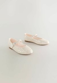 Mirdzoši beigtas Mary Jane vieglas kurpes ar apaļiem purngaliem, zemu papēdi un vienu siksniņu ar mazu sudraba sprādzi, izliktas uz neitrāla fona.