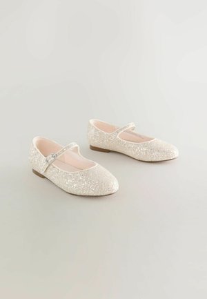 Glitzernde beigefarbene Mary Jane-Ballerinas mit runden Zehen, niedrigen Absätzen und einem einzelnen Riemen mit einer kleinen silbernen Schnalle, auf einem neutralen Hintergrund präsentiert.