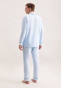 Ensemble de pyjama en coton bleu clair comprenant une chemise boutonnée avec col et manches longues, assortie d'un pantalon, le tout souligné d'un galon bleu foncé.