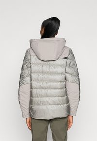 Giubbotto imbottito con finitura trapuntata grigio chiaro, cappuccio e pannelli sulle spalle in grigio liscio. Presenta un mix di texture e una vestibilità regolare.