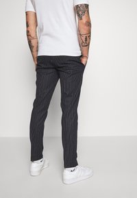 Granatowe spodnie w cienkie prążki o dopasowanym kroju, wykonane z gładkiej tkaniny, z bocznymi kieszeniami, zestawione z białymi sneakersami.