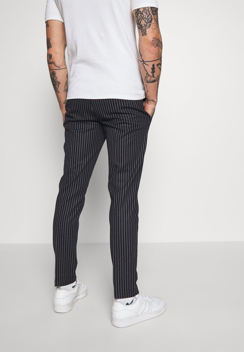 Granatowe spodnie w cienkie prążki o dopasowanym kroju, wykonane z gładkiej tkaniny, z bocznymi kieszeniami, zestawione z białymi sneakersami.