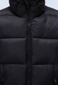 Czarna pikowana kurtka z wysokim kołnierzem, zapięciem na zamek z przodu oraz regulowanymi sznurkami przy kapturze. Gładka, błyszcząca faktura.