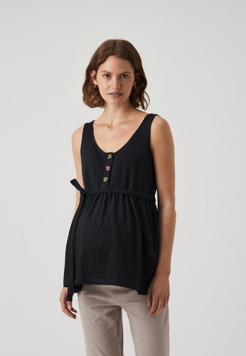 Top senza maniche nero con scollatura a V, bottoni frontali e vita cinchata legata con tessuto. Texture morbida, design casual. Abbinato a pantaloni chiari.