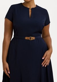 Abito blu navy con maniche corte e scollatura a chiave, caratterizzato da una cintura marrone con fibbia dorata, tessuto liscio e gonna svasata.