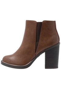 Stivale alla caviglia in eco-pelle marrone con inserti laterali elastici, punta rotonda e tacco nero impilato. Texture liscia con un leggero luccichio.