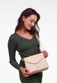 Béžová kožená crossbody taška s klopou, minimalistický design a malý logo akcent. Hladký povrch a nastavitelný popruh.