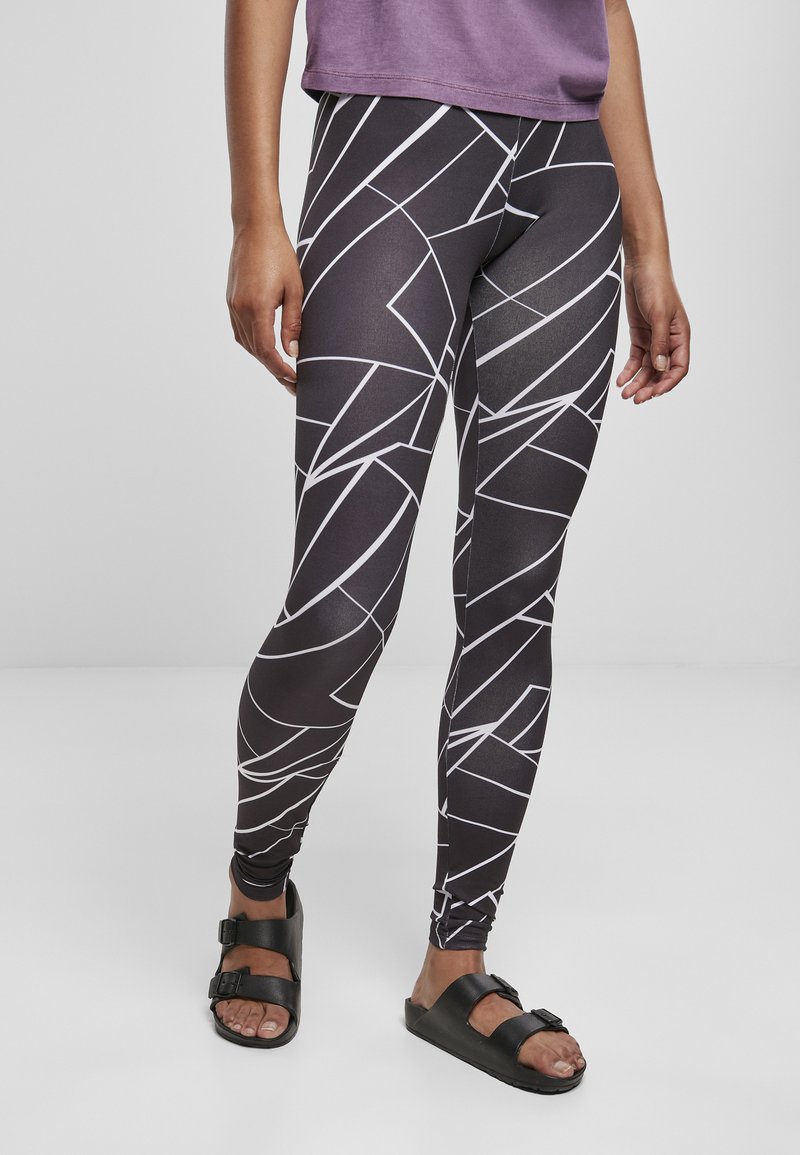 Leggings neri con un motivo geometrico bianco, realizzati in un tessuto elasticizzato. Abbinati a sandali neri e una maglietta viola.