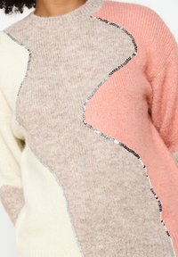 Knit sweater with a color-block design in beige, pink, and cream, featuring sequined accents along the seams. Textured, soft fabric.
