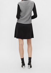 Grauer gerippter ärmelloser Pullover über einem schwarzen Kurzkleid, kombiniert mit kniehohen schwarzen Stiefeln mit transparenten Blockabsätzen.