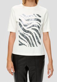 Vit bomull t-shirt med korta ärmar som har ett vågigt mönster av silver- och svarta paljetter. Matchas med svarta läderbyxor.