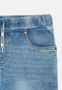 Pantalones vaqueros de mezclilla azul claro con una textura suave, que cuentan con una pretina, remaches de cobre y una etiqueta Levi's en la parte superior.