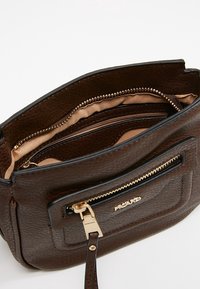 Ruskea nahkainen käsilaukku, jossa on teksturoitu pinta, kultaiset metalliosat, ylävetoketjusuljin ja useita sisätaskuja. Vuorattu pehmeällä beigevärisellä kankaalla.