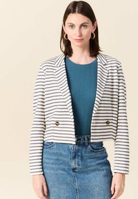 Blazer cropped a righe bianco e navy, con due bottoni dorati, colletto a risvolto e maniche lunghe, abbinato a un top teal a costine e una gonna in denim.
