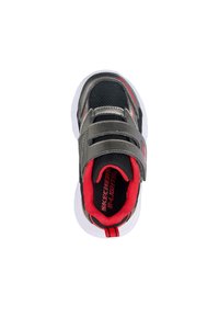 Zapatilla deportiva negra y gris con dos cierres de velcro, forro rojo, suela blanca y detalles de diseño mínimos. Suela de goma para tracción.