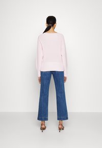 Ljusrosa stickad tröja med avslappnad passform, tillsammans med högmidjade blå utställda jeans och bruna klacksandaler. Enkel design utan mönster.