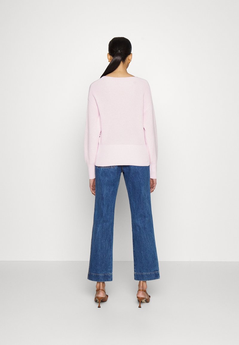 Ljusrosa stickad tröja med avslappnad passform, tillsammans med högmidjade blå utställda jeans och bruna klacksandaler. Enkel design utan mönster.