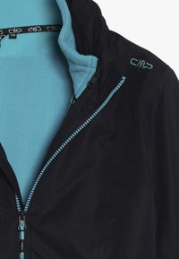 Sort jakke med et teal fleecefor, der har en frontlynlås med en teal detalje og et logo i hjørnet. Glat stoftekstur.