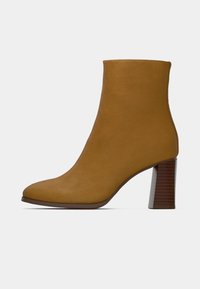 Barna színű szarvasbőr bokacsizma hegyes orral és vastag, fa mintázatú sarokkal. Sima textúrájú, varrással díszített felsőrésze van.