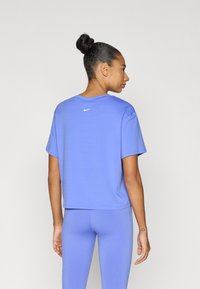 Μωβ κοντομάνικο τοπ με κοντά μανίκια, με λευκό λογότυπο Nike τυπωμένο στο πάνω μέρος της πλάτης, σε συνδυασμό με αντίστοιχο κολάν.