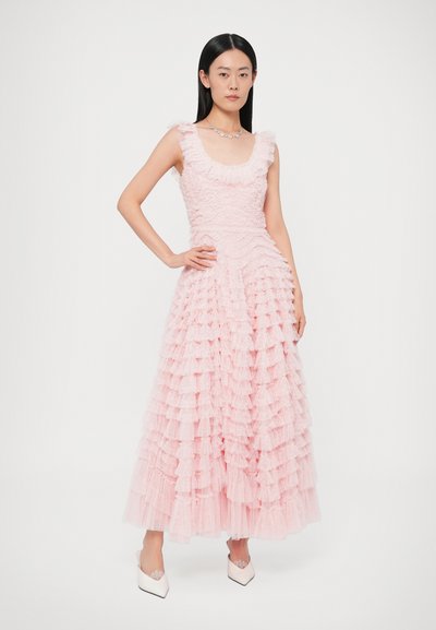 Rózsaszín fodros maxi ruha texturált anyagból, lekerekített nyakkivágással és fodros rétegekkel. A modell fehér hegyes orrú lapos cipőt visel.